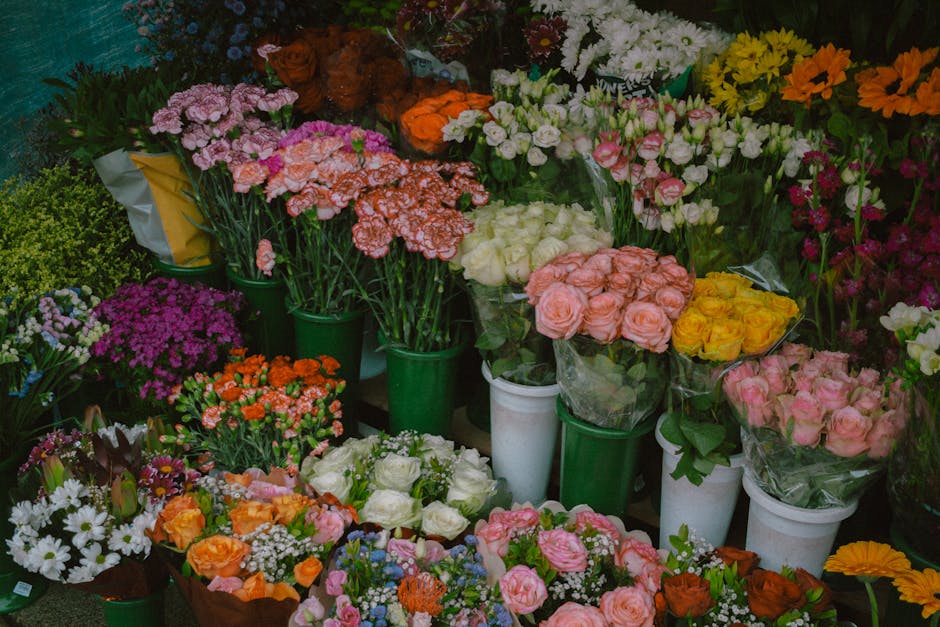 A vibrant display of various fresh flowers arranged in several green and white buckets and vases at Petts Wood Florist. The bouquet arrangement includes pink roses, yellow roses, white roses, and clus